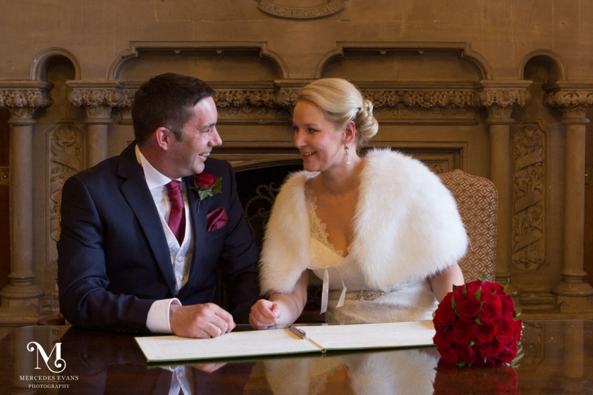 the newly weds sit and sign the register in front of the fireplace in the Oak room at the Elvetham