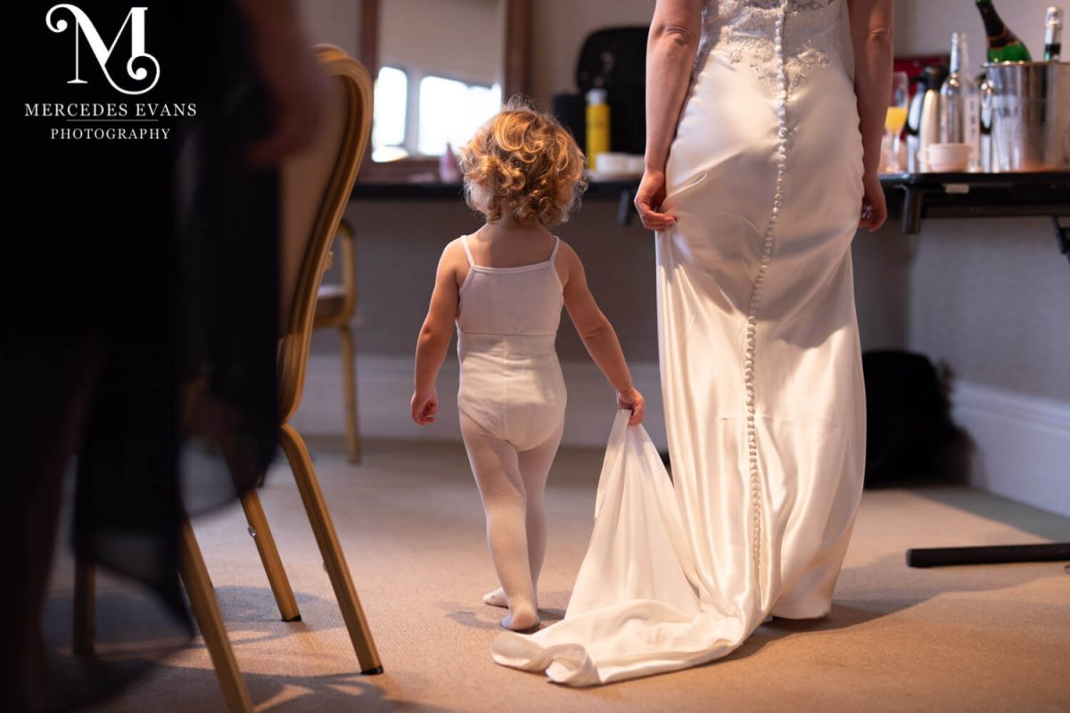 the little flower girl practises holding the bride's wedding dress train in the hotel room before the ceremony