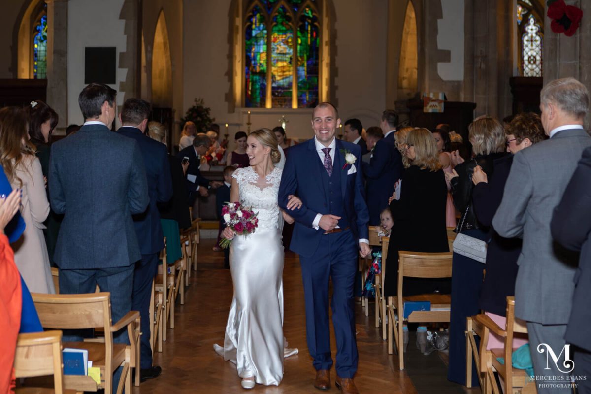 the new spouses walk happily back down the aisle, as they smile at their wedding guests in church