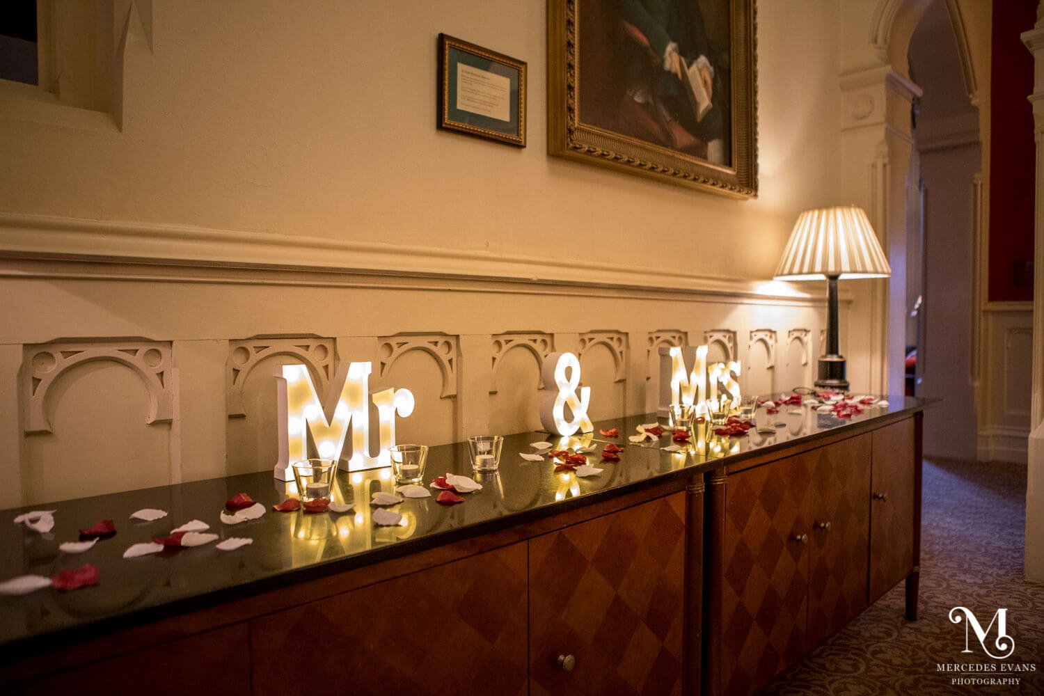 Mr & Mrs lit up letters along with rose petals on a cabinet at the wedding