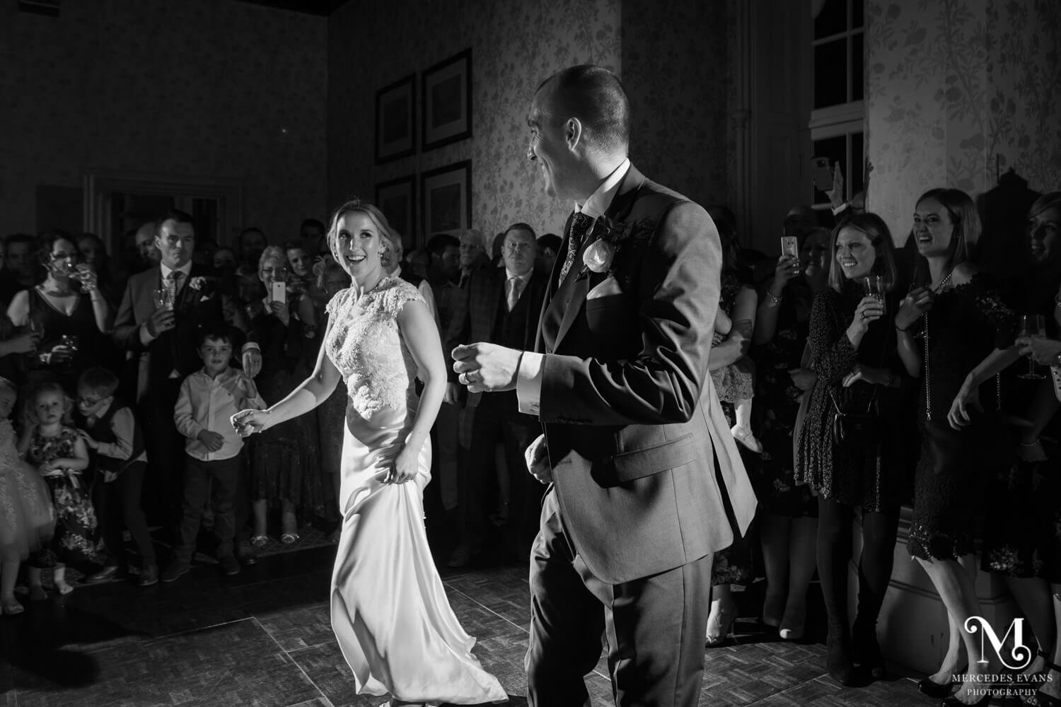 a black and white photo of the bride and groom laughing as they dance their first dance