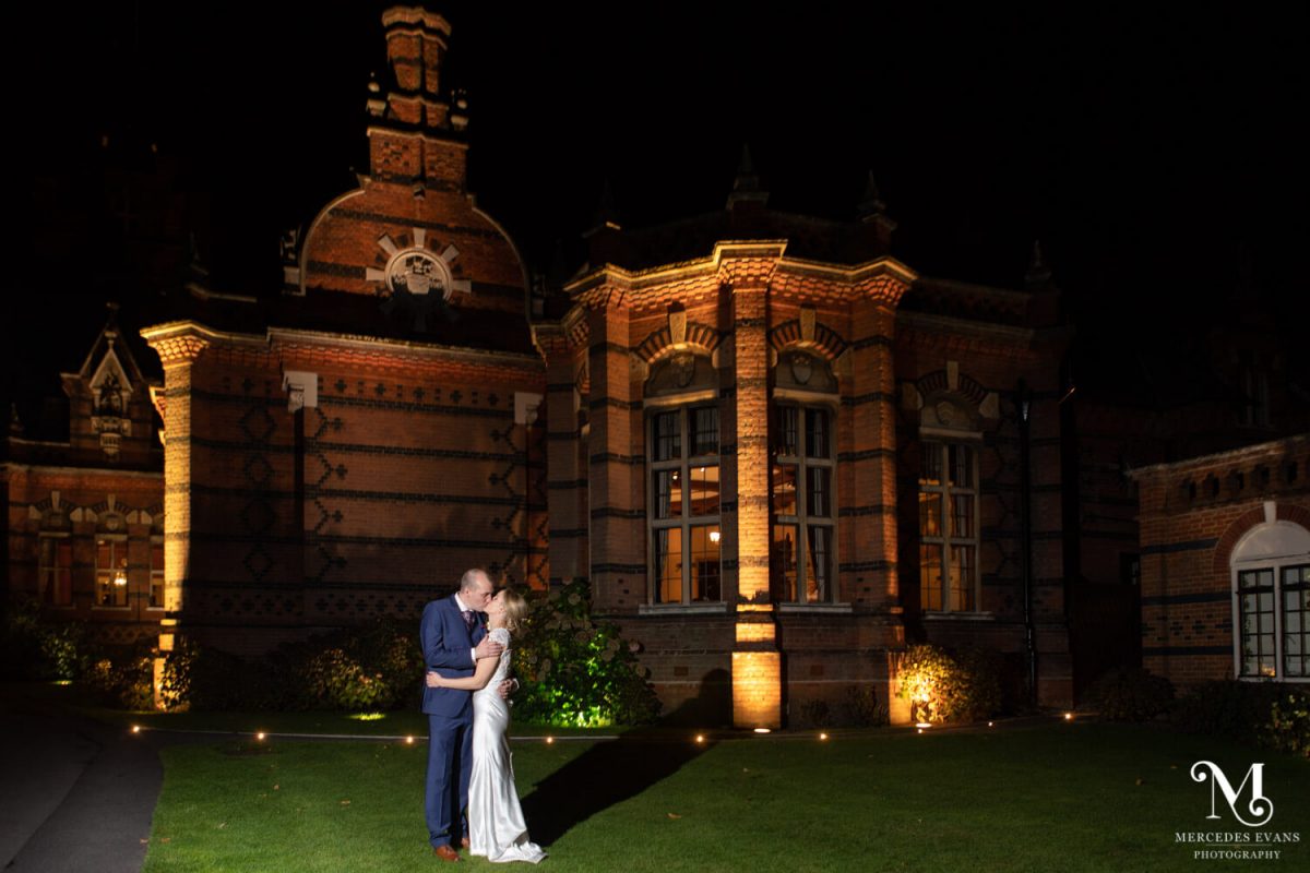 the bride and groom kiss outside the Elvetham at the end of the night. The couple and the building are lit up