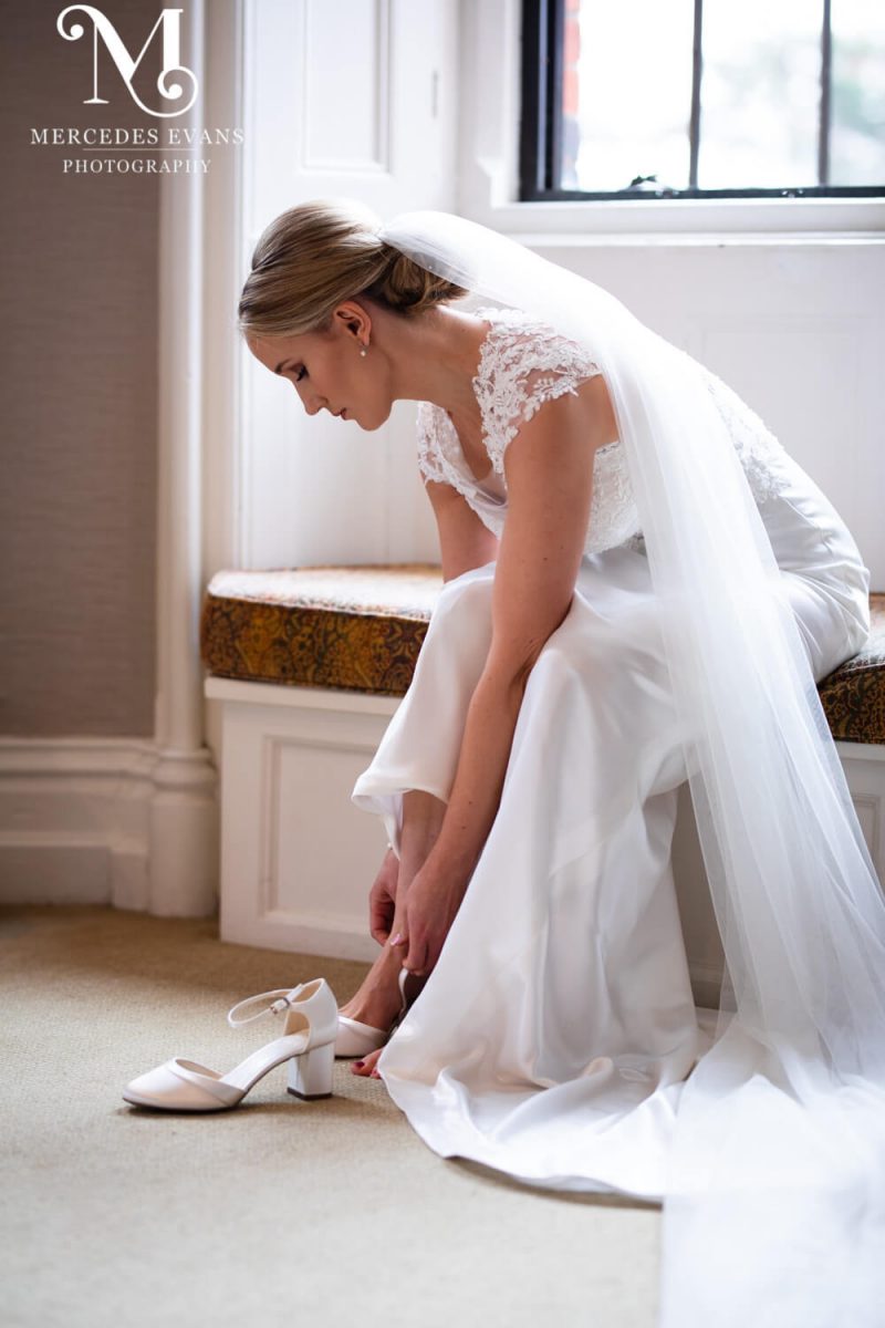 the bride sits in a window seat and puts on her shoes in the Seymour room at the Elvetham