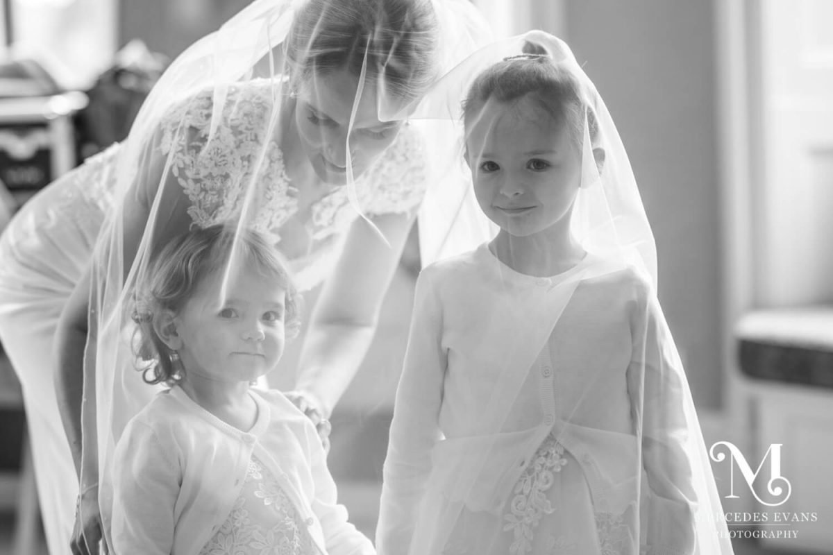 the bride and her two flower girls stand together underneath her wedding veil