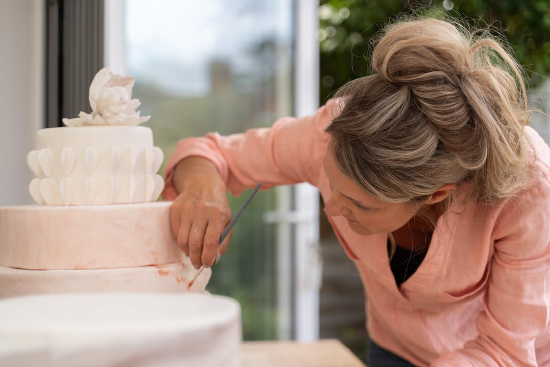 A professional cake maker paints a three tier wedding cake in her conservatory during her branding photo shoot