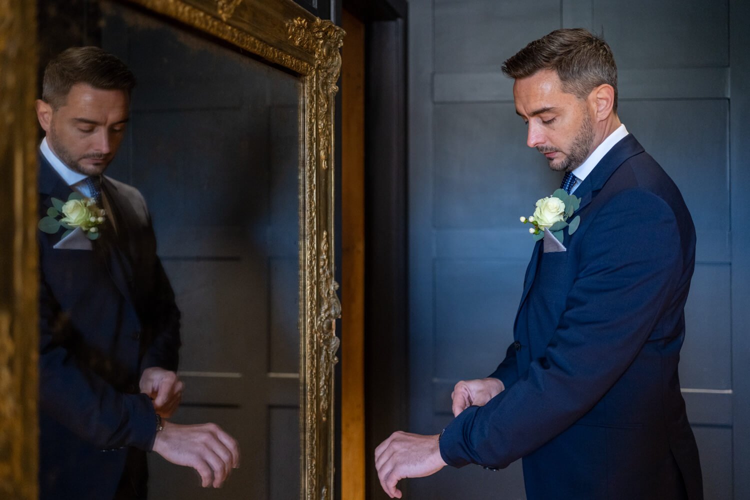 groom rearranges his cuff as he stands in front of the mirror before the wedding