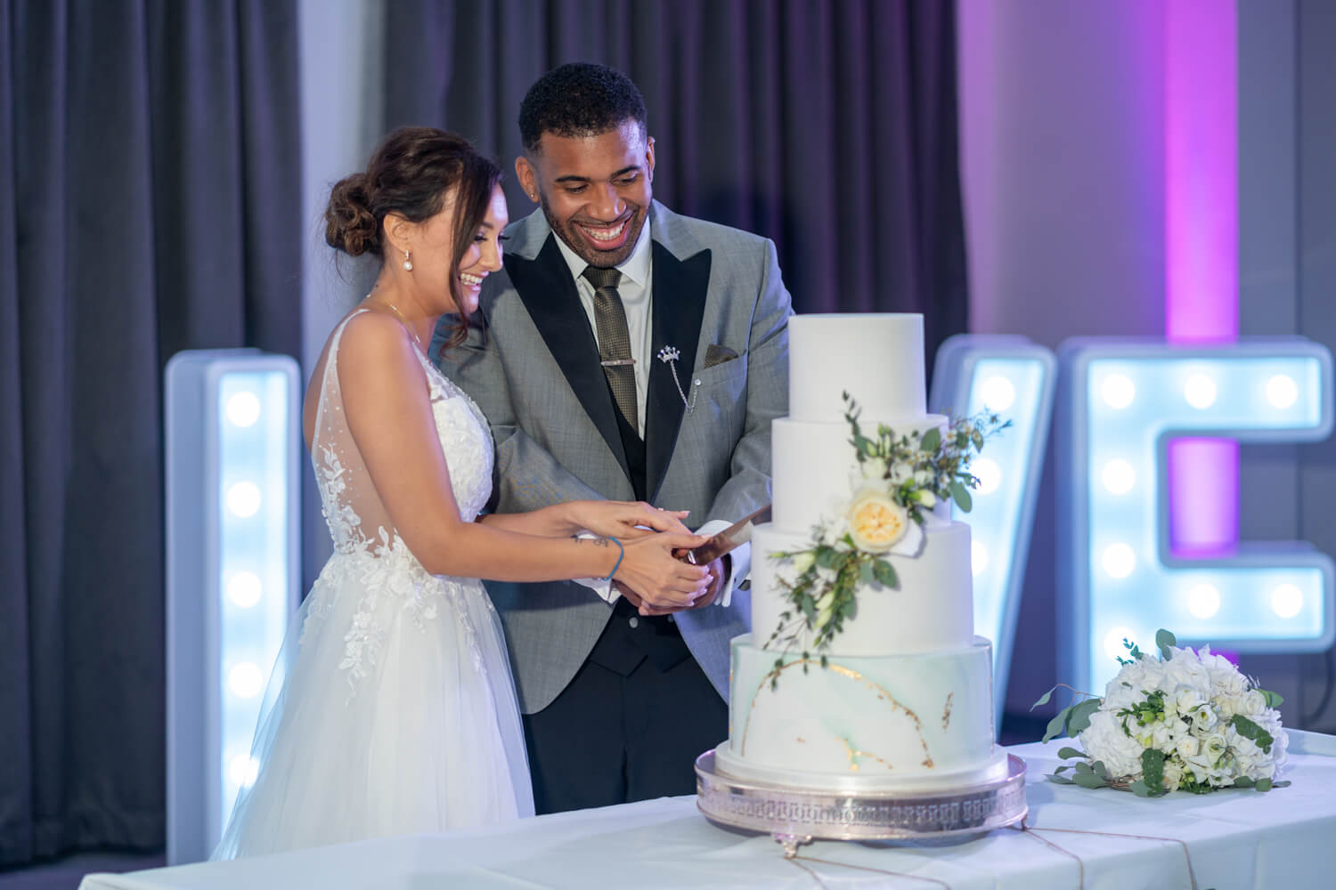 bride and groom cut the cake with love letters lit up behind them