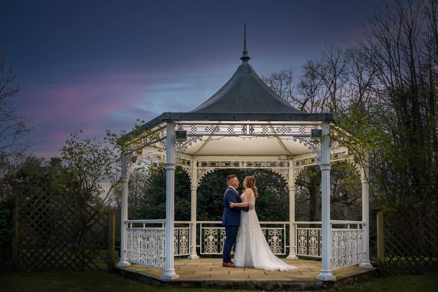 The backlit bride and groom embrace under the pergola at Farnham House Hotel during dusk