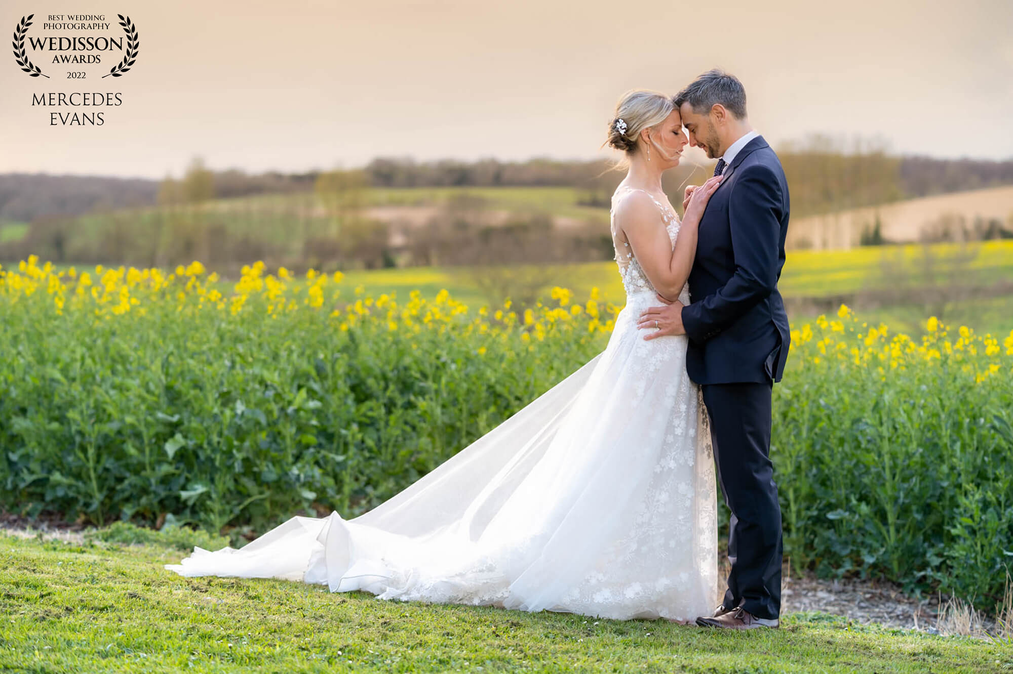 Bride and groom embrace by the rapeseed field at Bury Court Barn during golden hour
