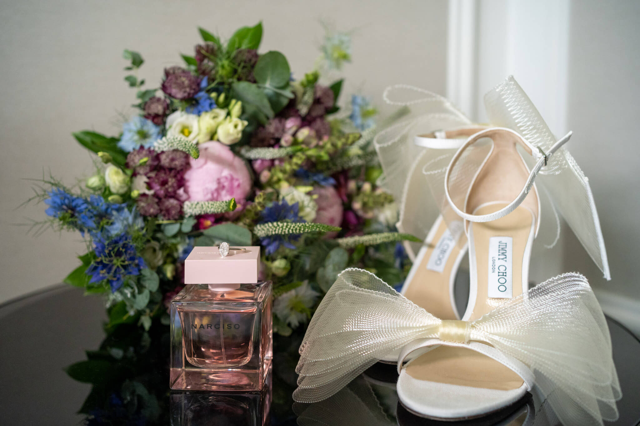 Bride's Jimmy Choo stilettos with huge bows next to her Narciso perfume, engagment ring and bouquet