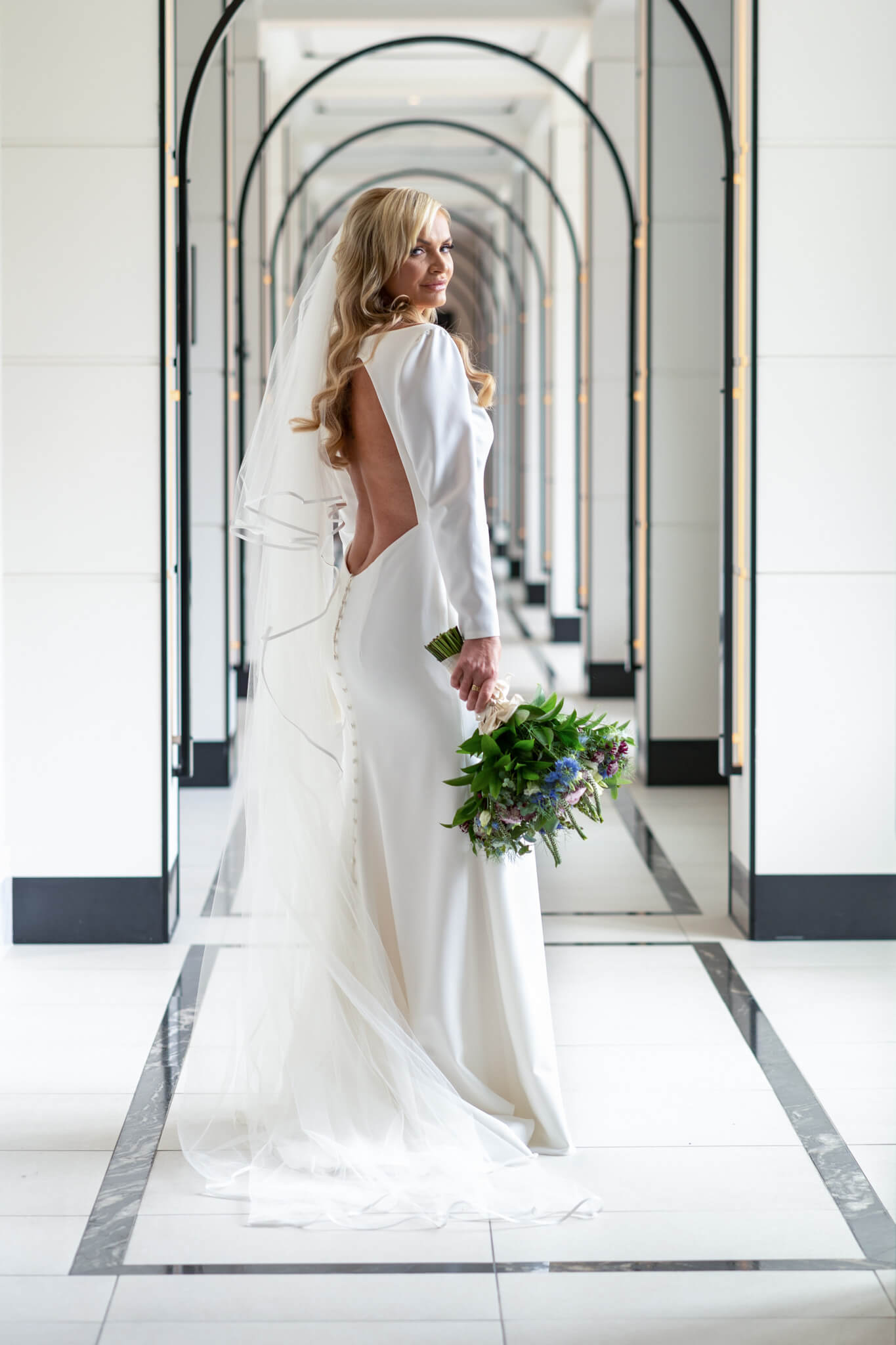 blonde long haired bride stands looking over her shoulder in the corridor at the Fairmont Windosr Park