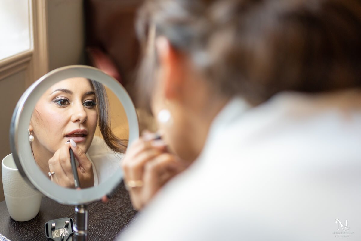 the bride fixes her lipstick as she looks into a round mirror