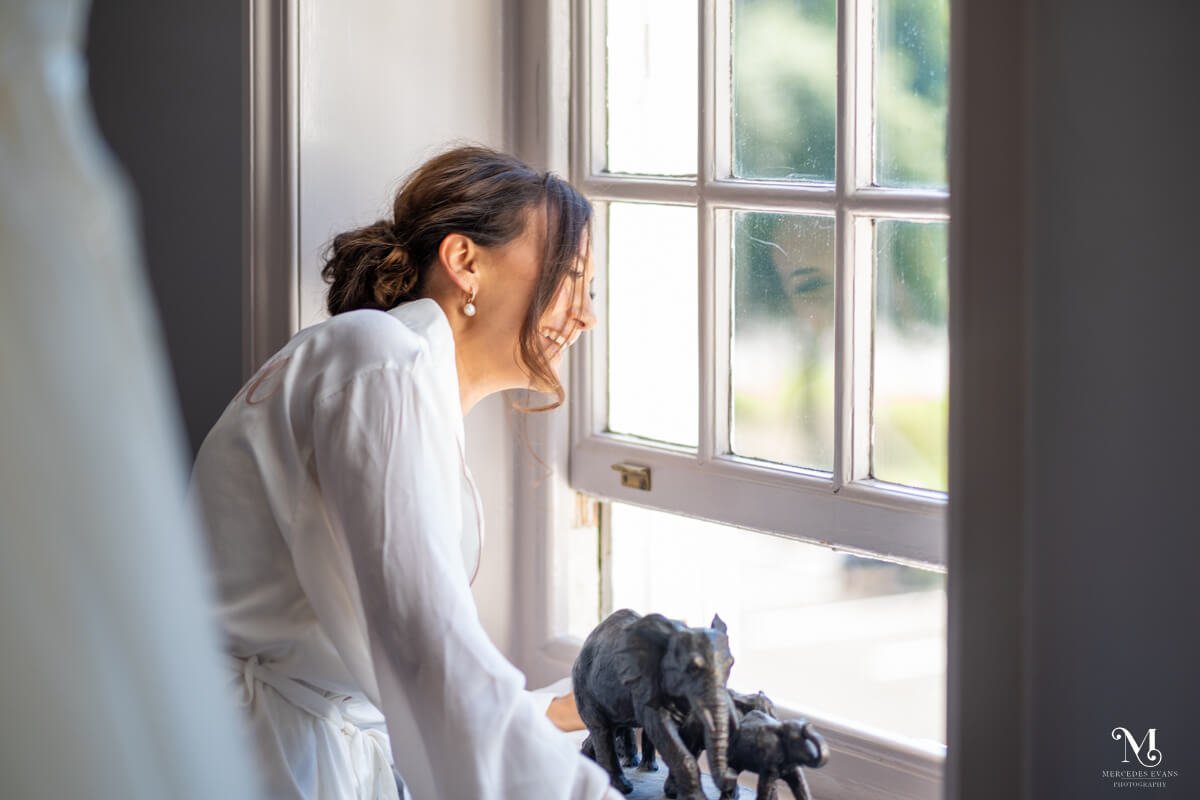 the bride laughs and looks out of the hotel window as the guests arrive downstairs at the hotel