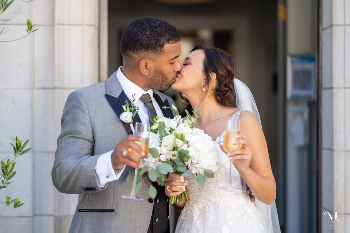 the bride and groom share a kiss as they stand holding their glasses of champagne of the front doorstep of gorse hill hotel