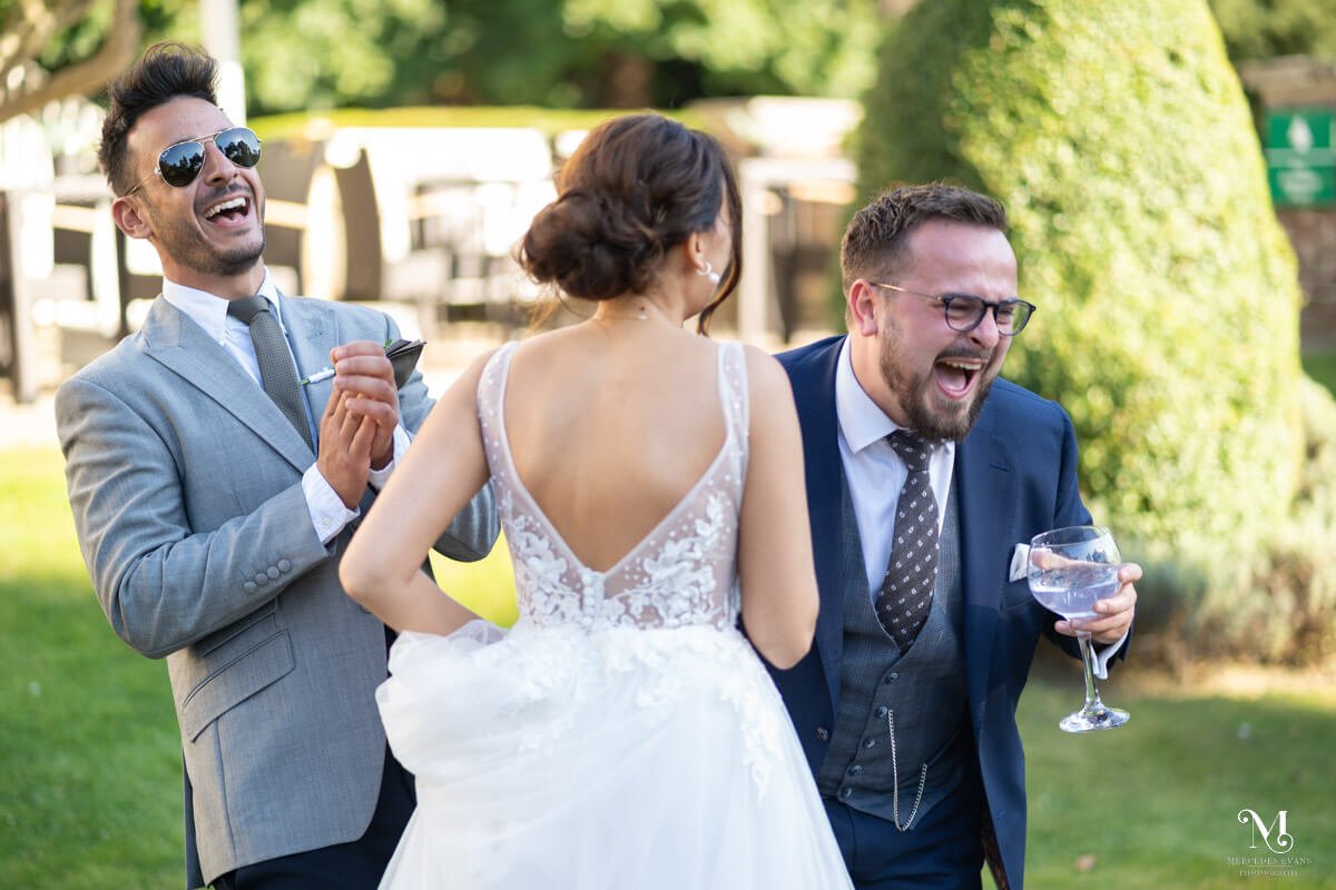 wedding guests laugh hysterically with the groom in the gardens at Gorse hill