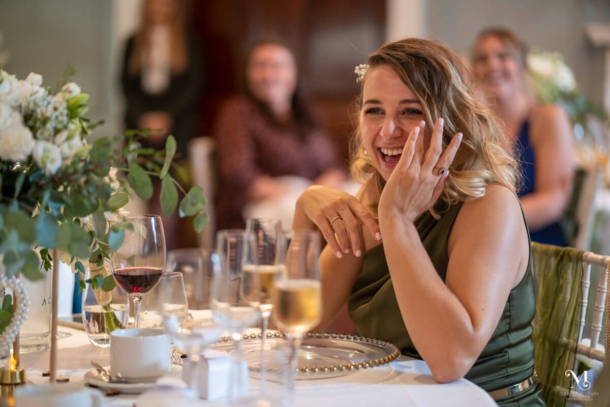 a bridesmaid wipes away her tears of laughter as she sits and enjoys the wedding speeches
