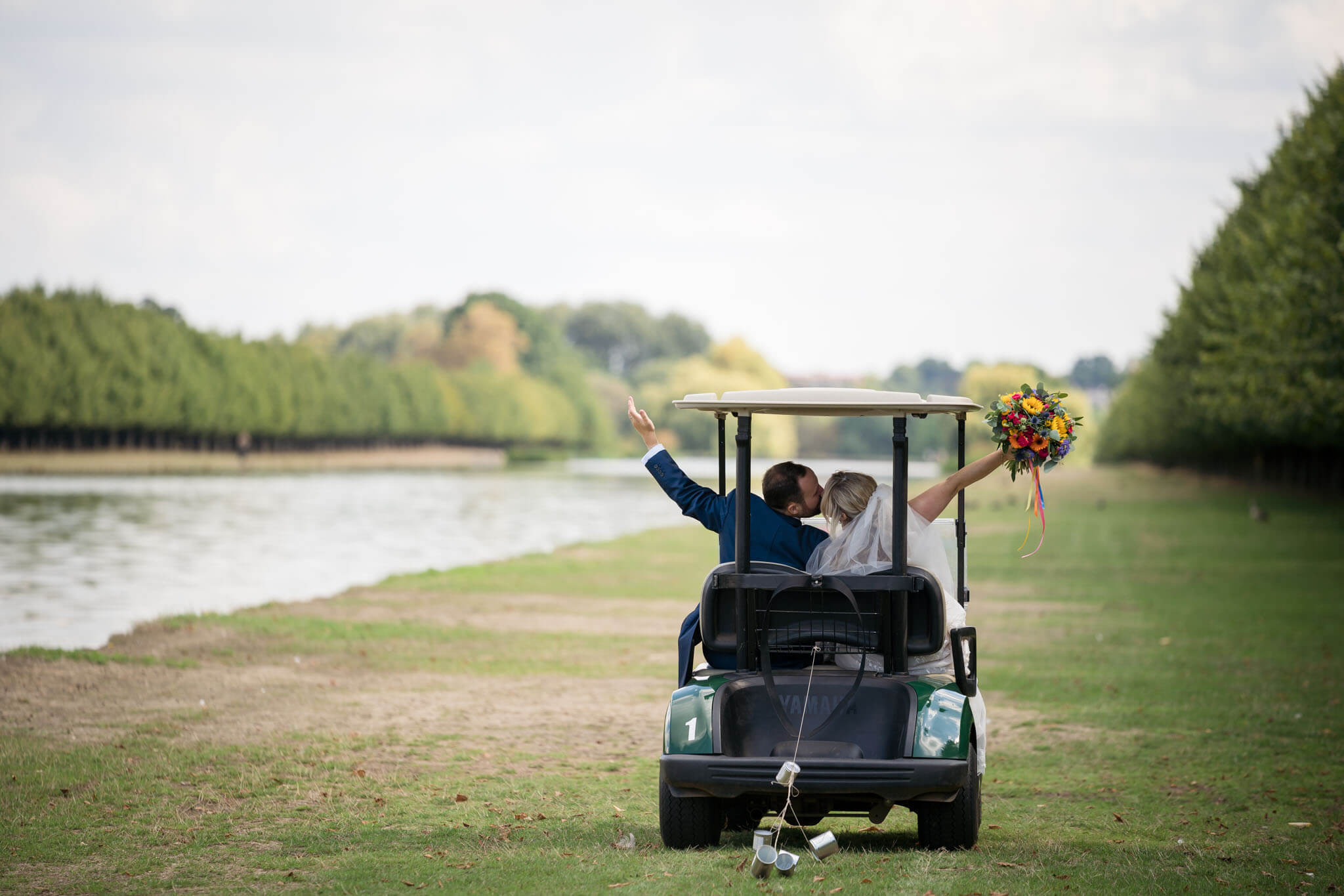 bride and groom celebrate with a kiss as they drive away in a golf buggy the grounds of Hampton Court Palace Golf Club