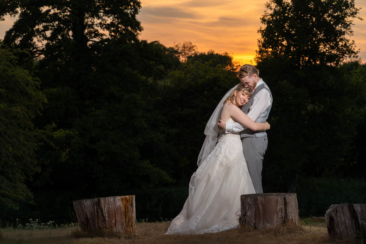 the bride and groom stand embracing each other at sunset at norman court barn