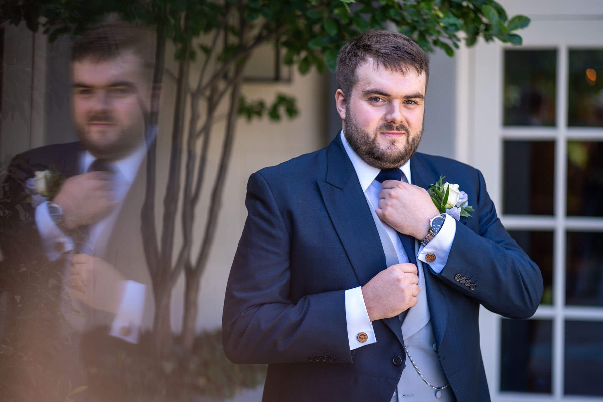 the groom wearing a blue suit ad grey waistcoat straightens his tie