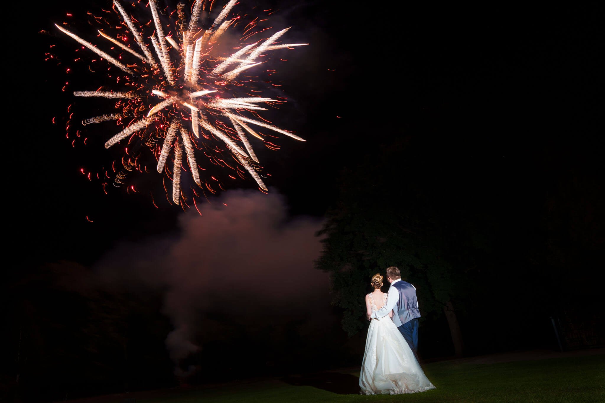 bride and groom stand together watching the fireworks