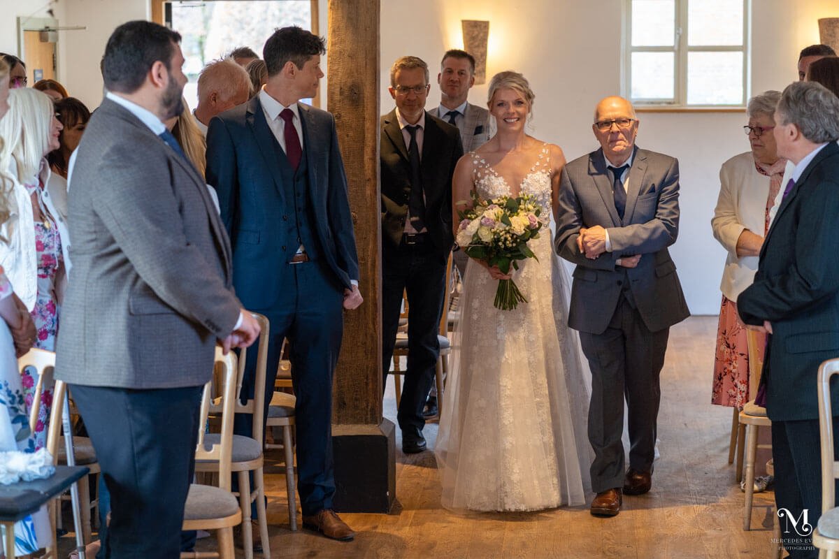 the bride walks up the aisle on the arm of her father, as guests look on