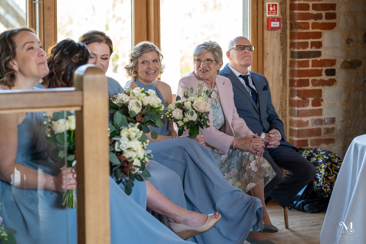 the parents of the bride and bridesmaids laugh together as they sit during the wedding service