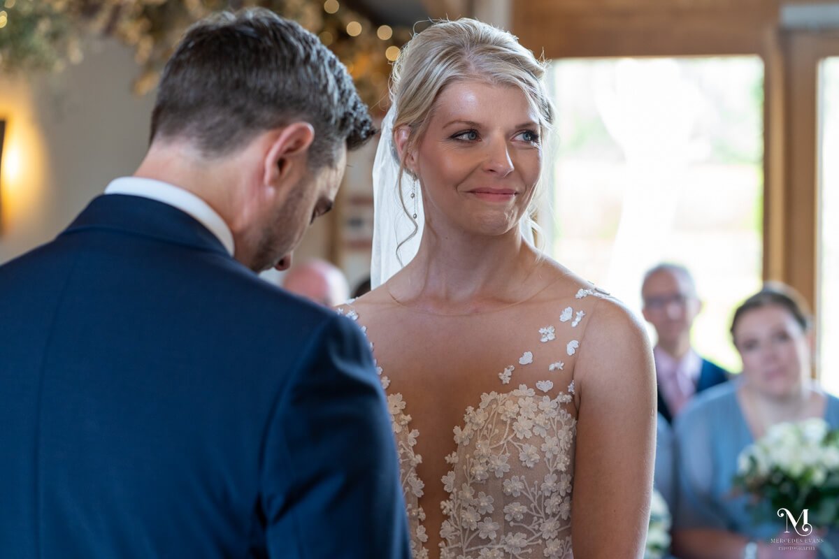the bride smiles at the officiant as the groom bows his head and holds back tears