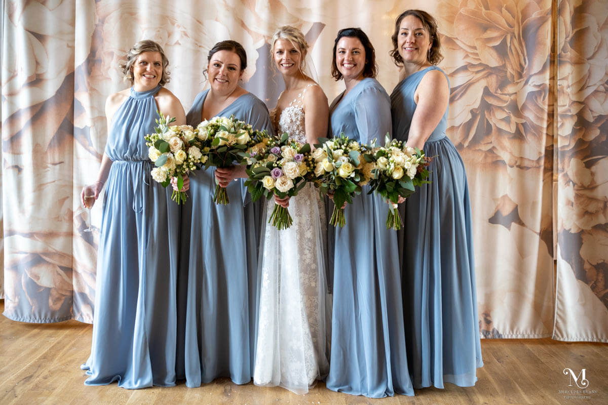 the bride poses in a line with her bridesmaids for a formal photograph