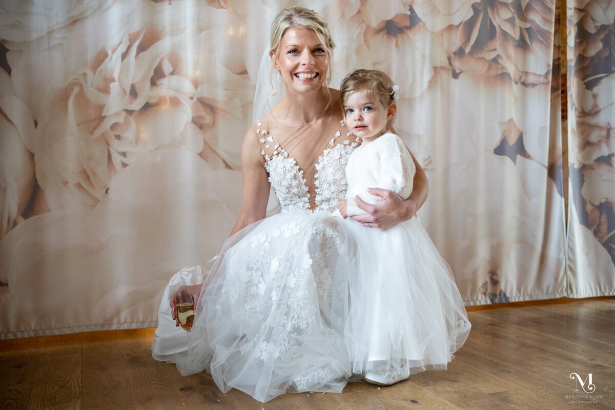 the smiling bride crouches down next to the little flower girl