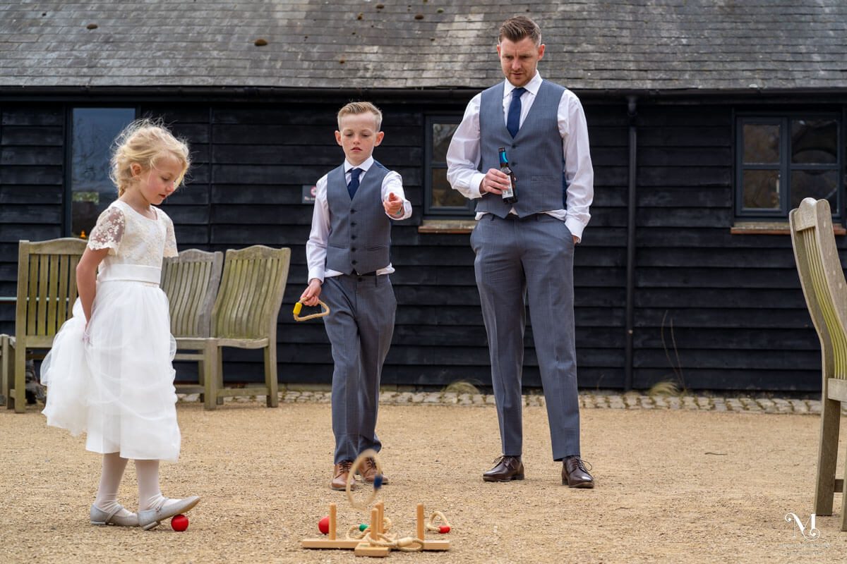 a young boy throws a rope ring as he plays quoits with his father and flower girl sister