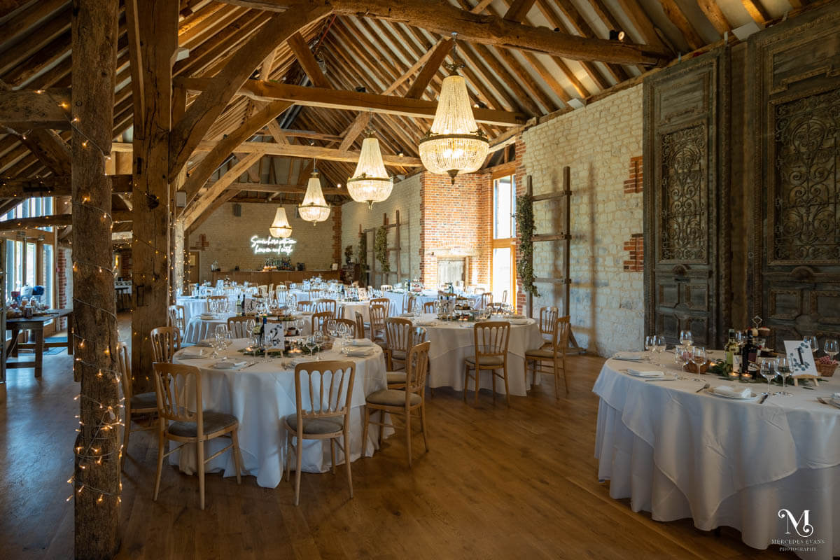 The Barn at Bury Court lit with chandeliers and laid for an afternoon tea wedding breakfast