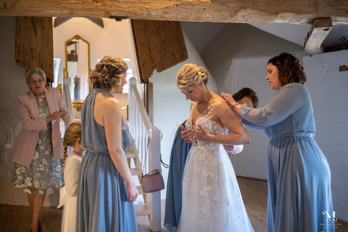 the bridesmaids help the bride into her wedding dress