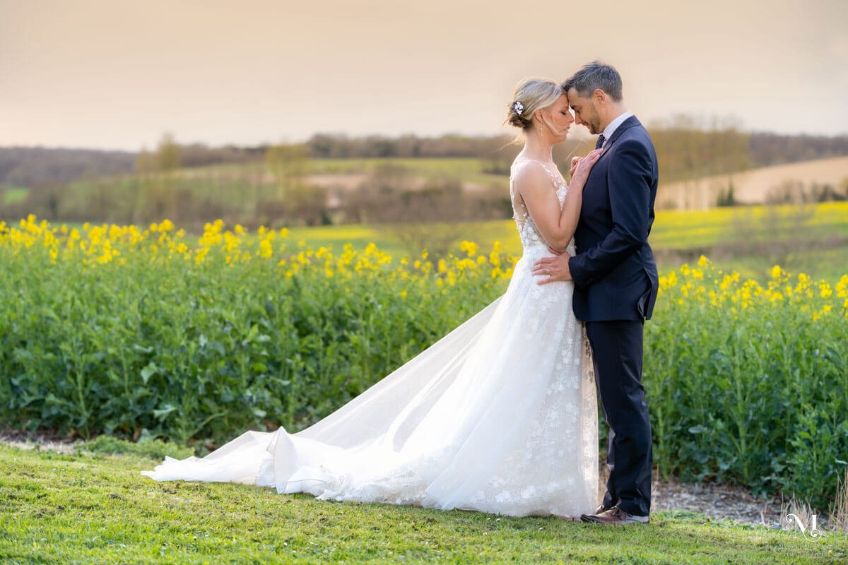 bride and groom stand with heads together in front of a flowering rapeseed field