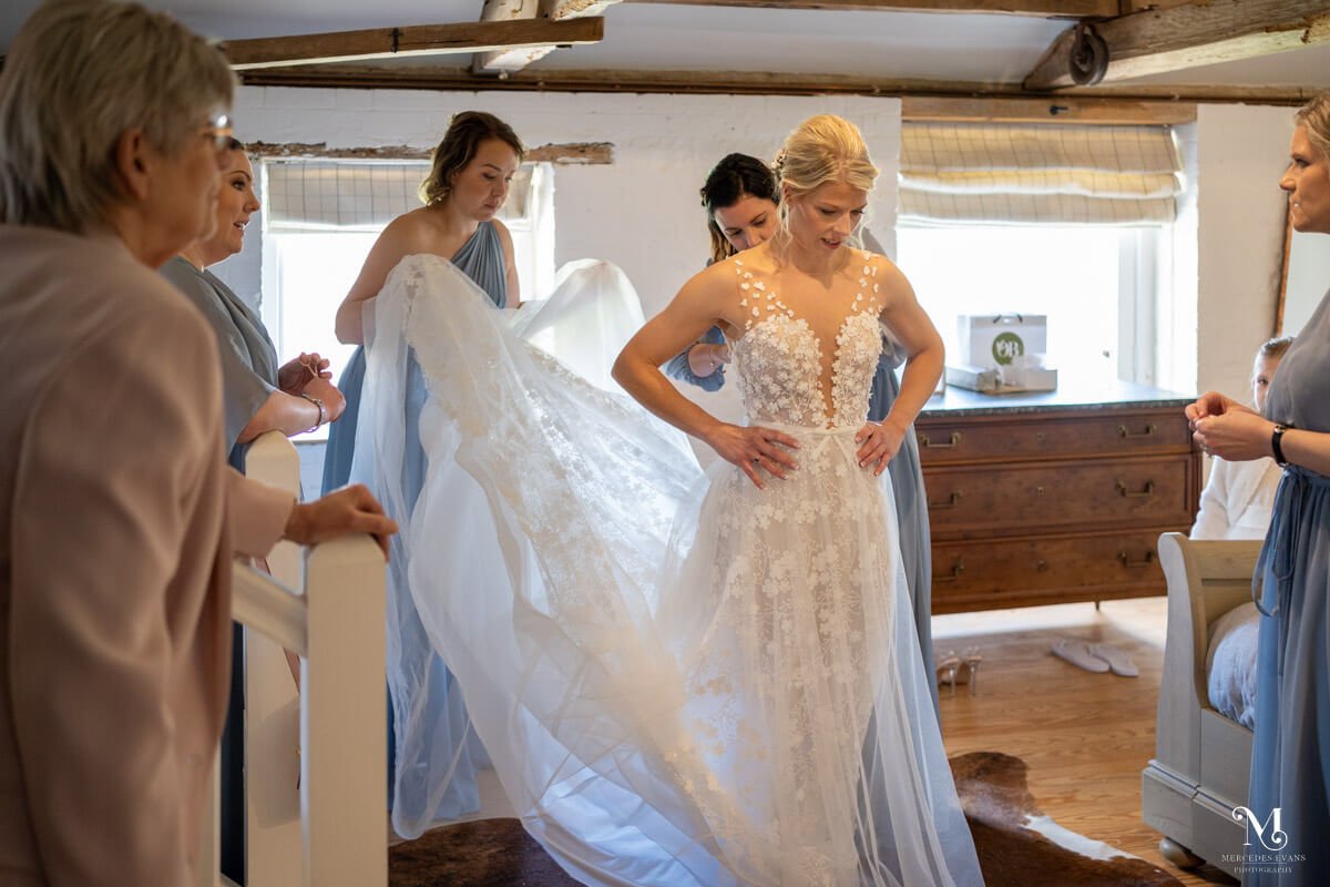 the bridesmaids fluff out the bride's dress as she gets ready