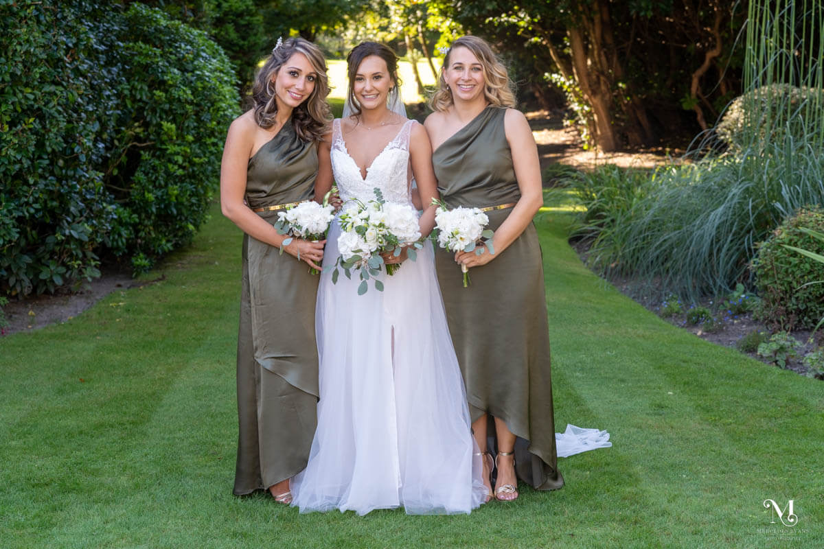the bride and her two bridesmaids stand in a green garden