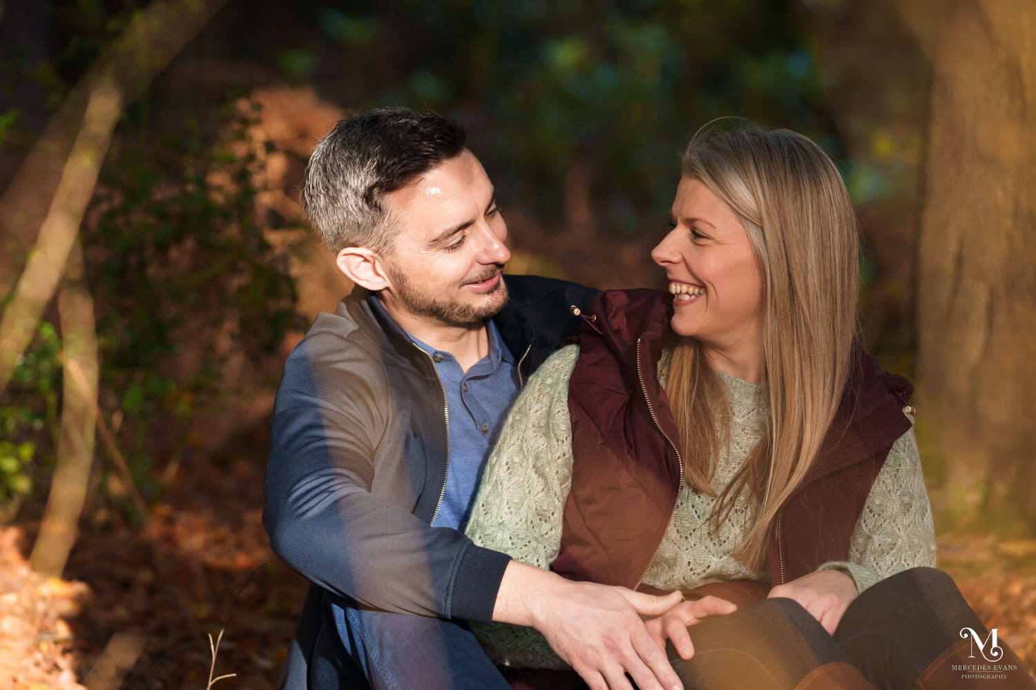bride and groom sit in an autumnal wood and laugh together