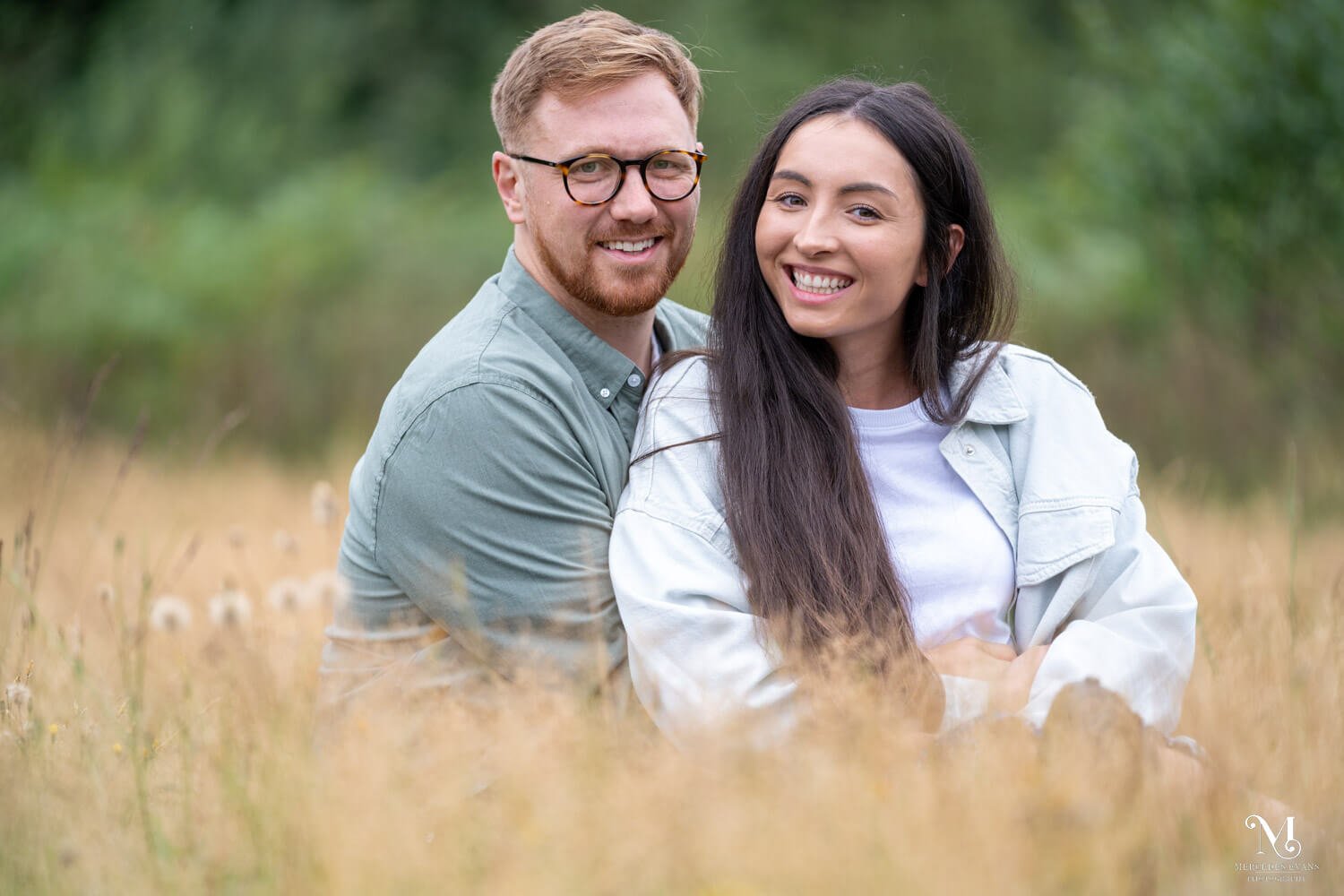a smiling couple sit together in long golden grass