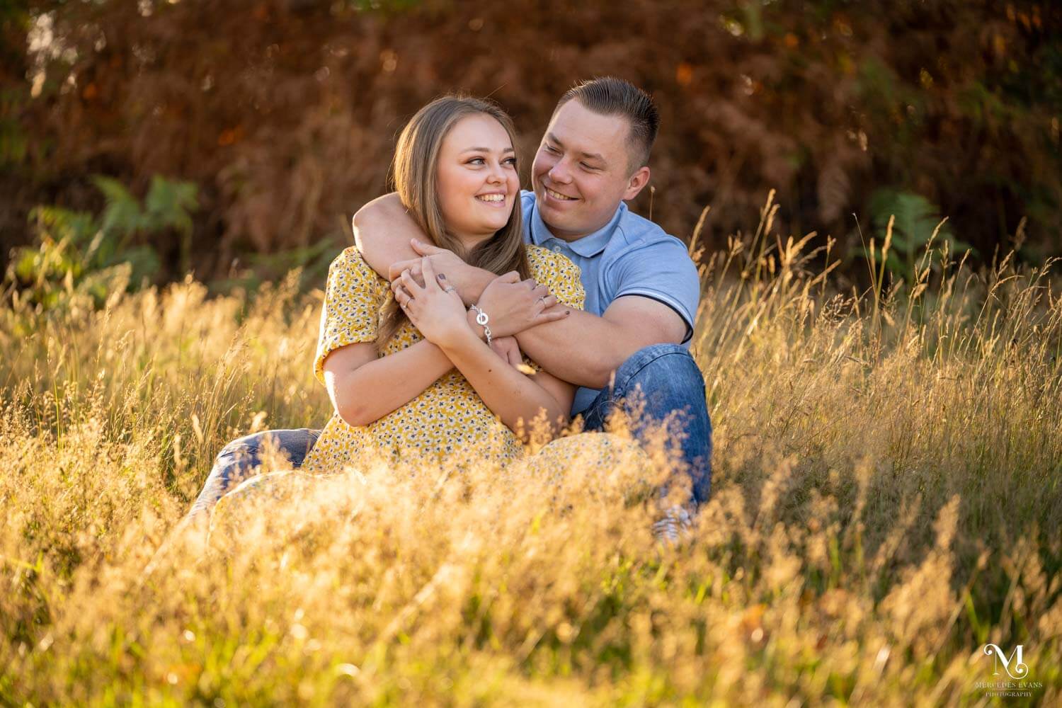 young couple sit together in the long grass during golden hour