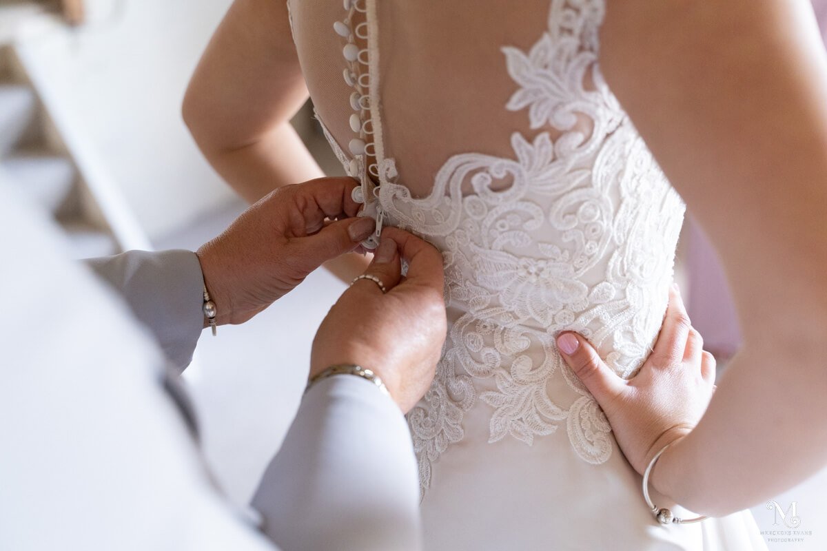 a detail shot of the mother of the bride's hands as she does up the bride's buttons on the back of her wedding dress