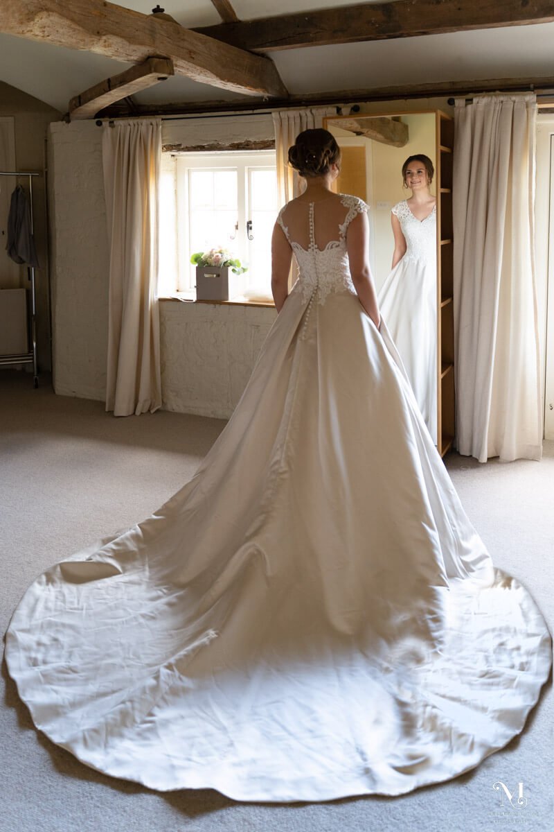 the bride looks at her reflection in the mirror and her wedding dress train is spread out behind her