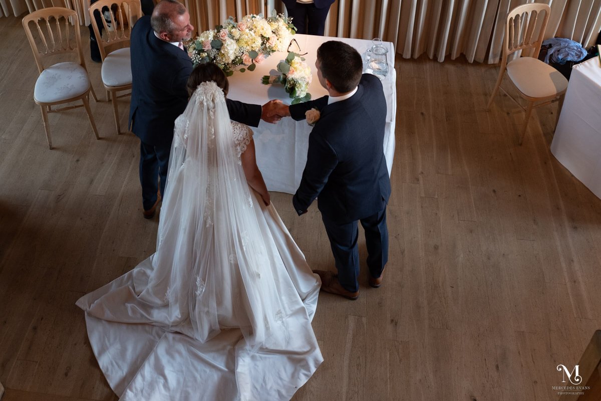 an aerial view of the groom shaking hands with the father of the bride at the top of the aisle, the bride stands between them both
