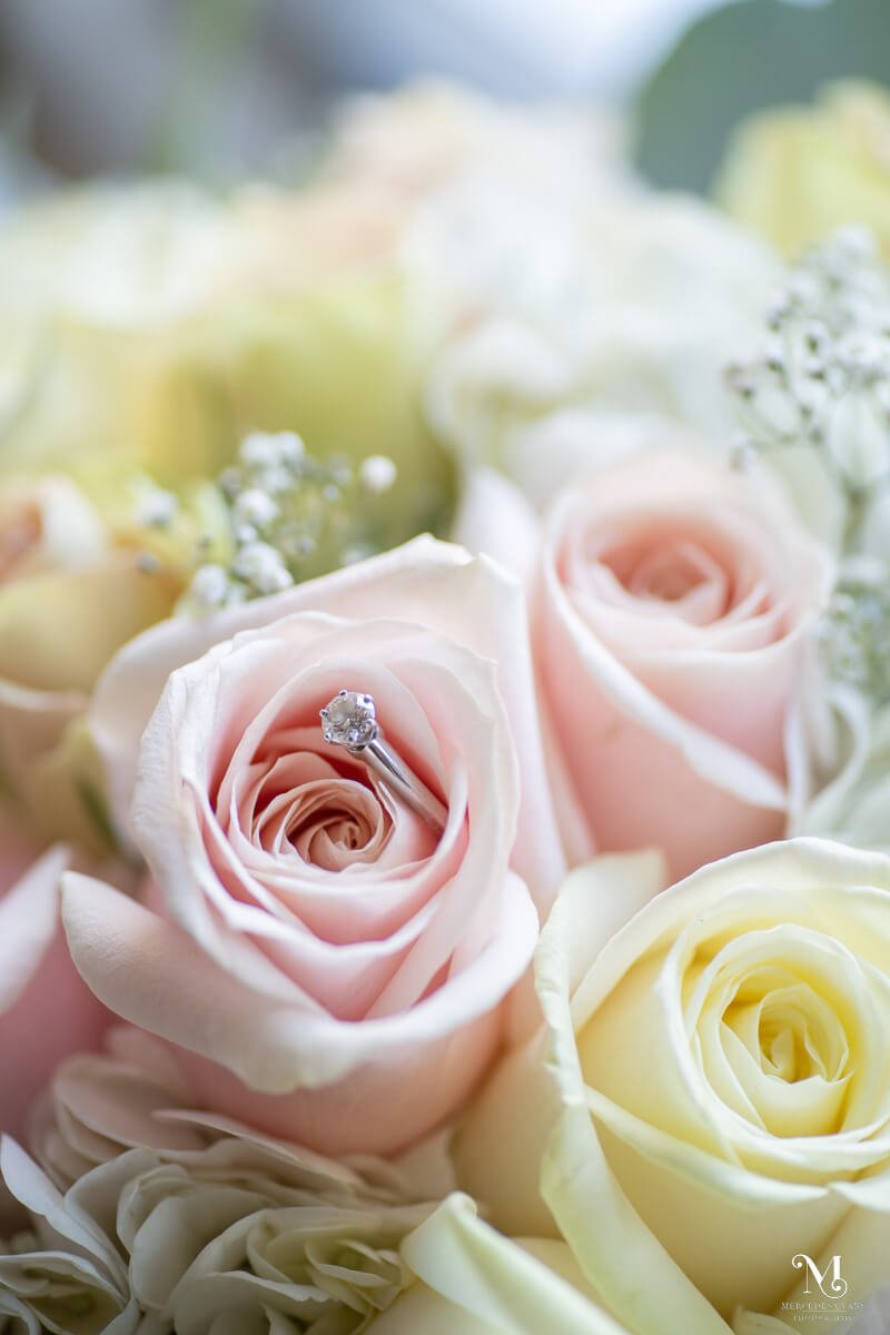 a diamond engagament ring nestled in a bouquet of pink and yellow roses and gypsophilia
