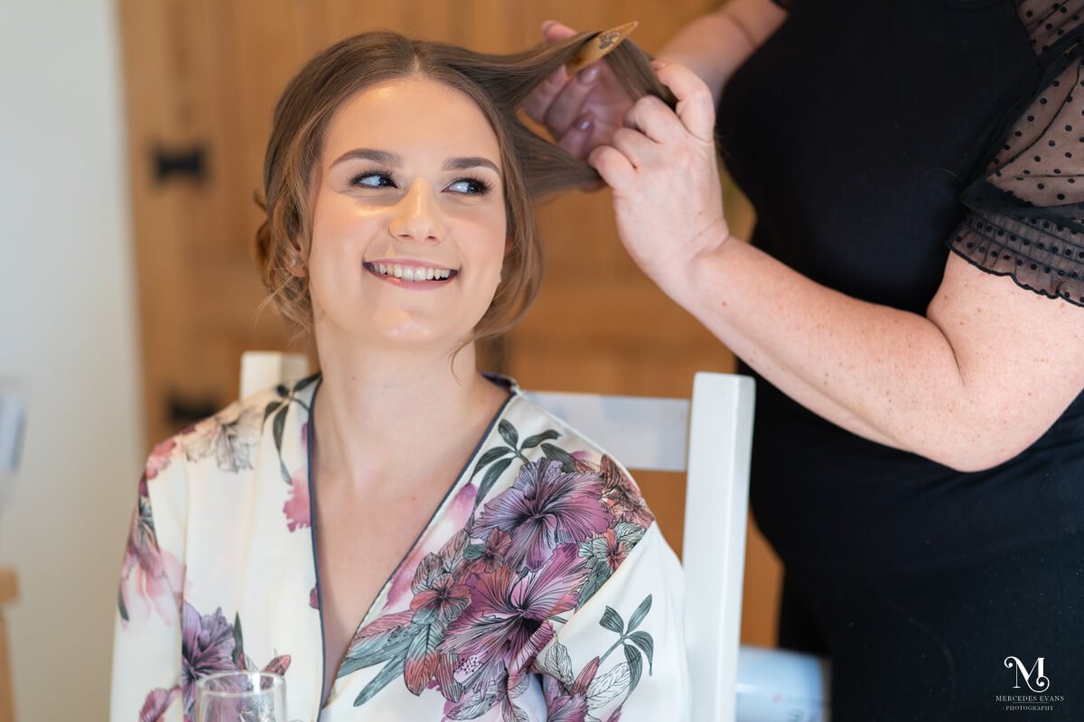 a bride wearing floral pyjamas smiles and looks at someone to her side as she has her hair done