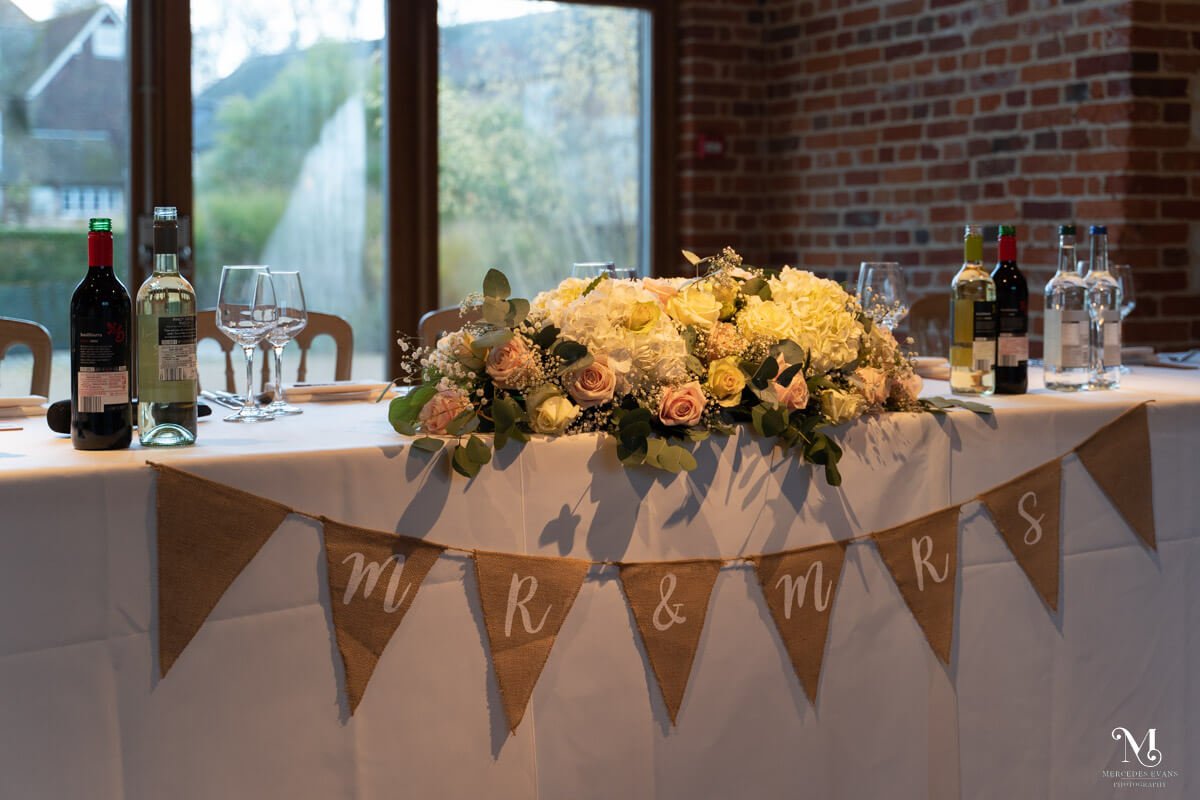 the top table in front of the window, decorated with pink, yellow and white flowers and a Mr and Mrs banner