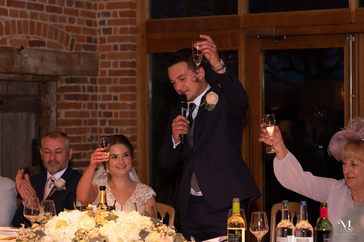 the groom and top table raise a glass and clap during his speech