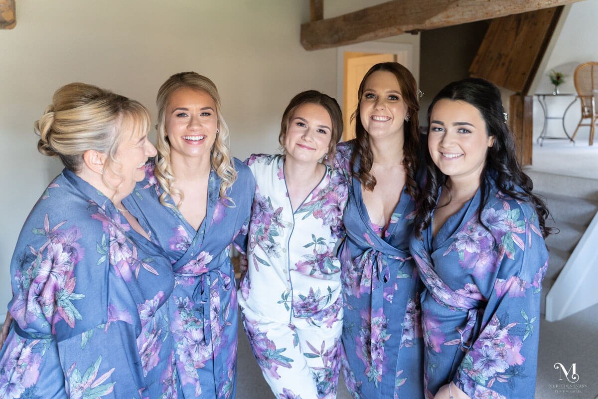 the bride wearing white floral pyjamas and her four bridesmaids wearing matching blue floral dressing gowns laugh together