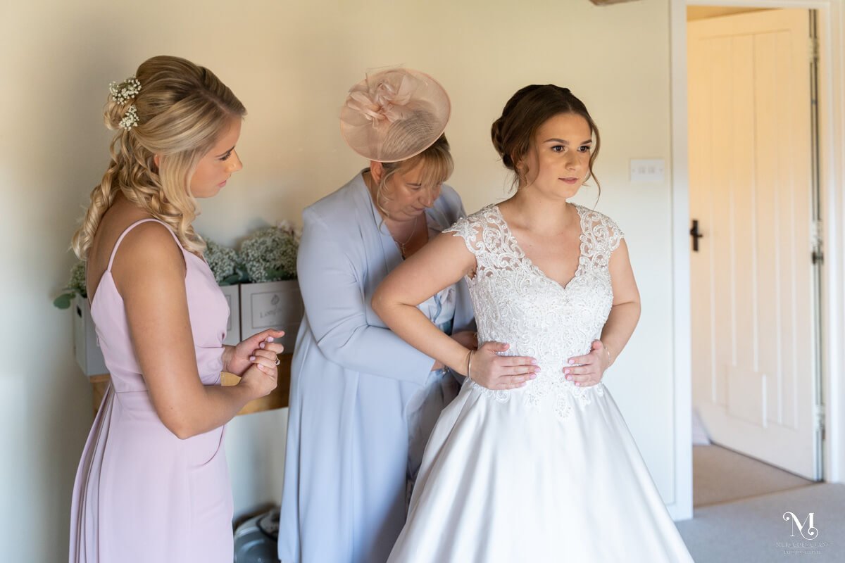 the mother of the bride does up the buttons on the bride's wedding dress and bridesmaid watches on