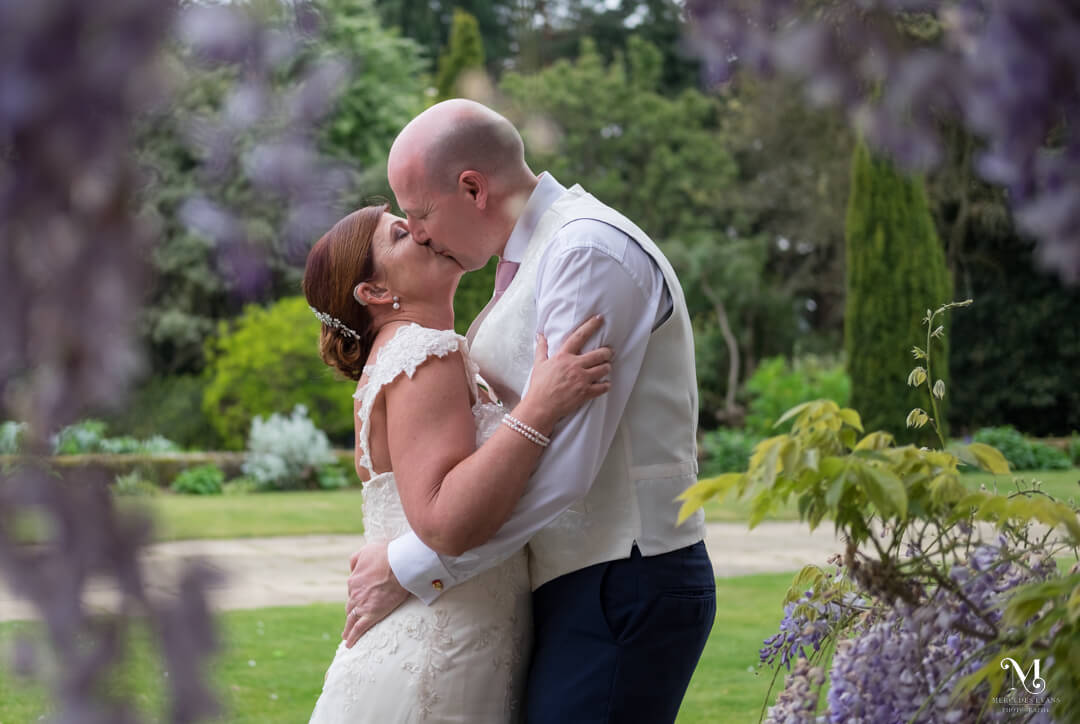 the bride and groom kiss next to a wisteria clad building