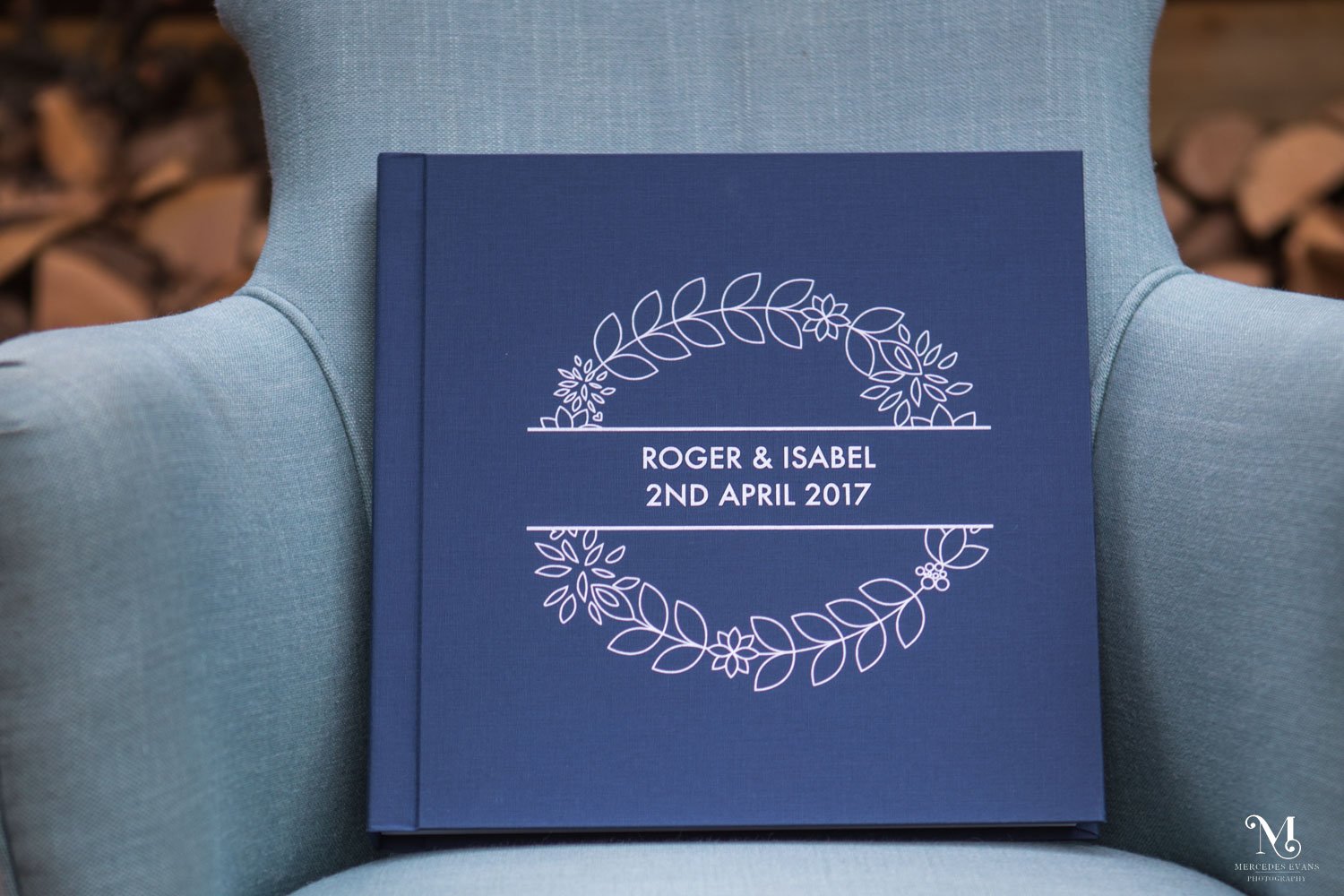 navy blue wedding album sits upright on a pale blue arm chair outside