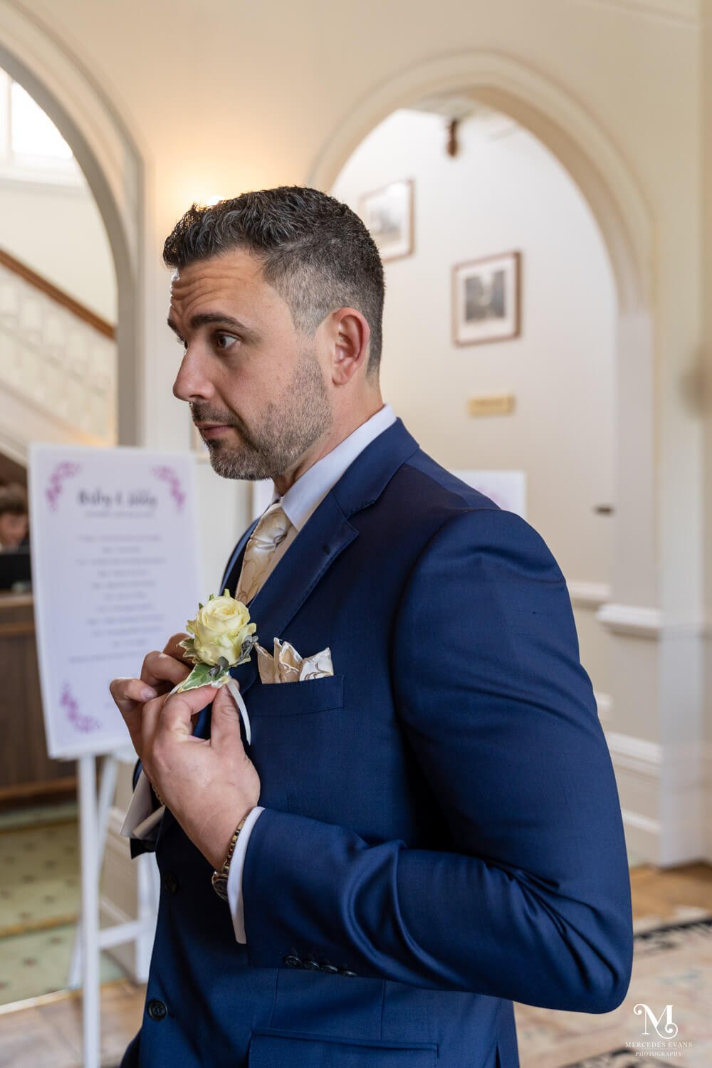 the groom puts on his buttonhole in front of the mirror in the hallway of cantley house hotel